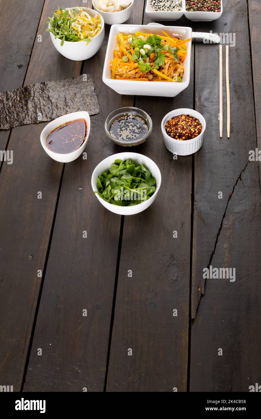 Blick von oben auf den asiatischen Wok, in dem Nudeln mit Essstäbchen, Löffel und Gewürzen auf Holz gebraten werden Stockfoto