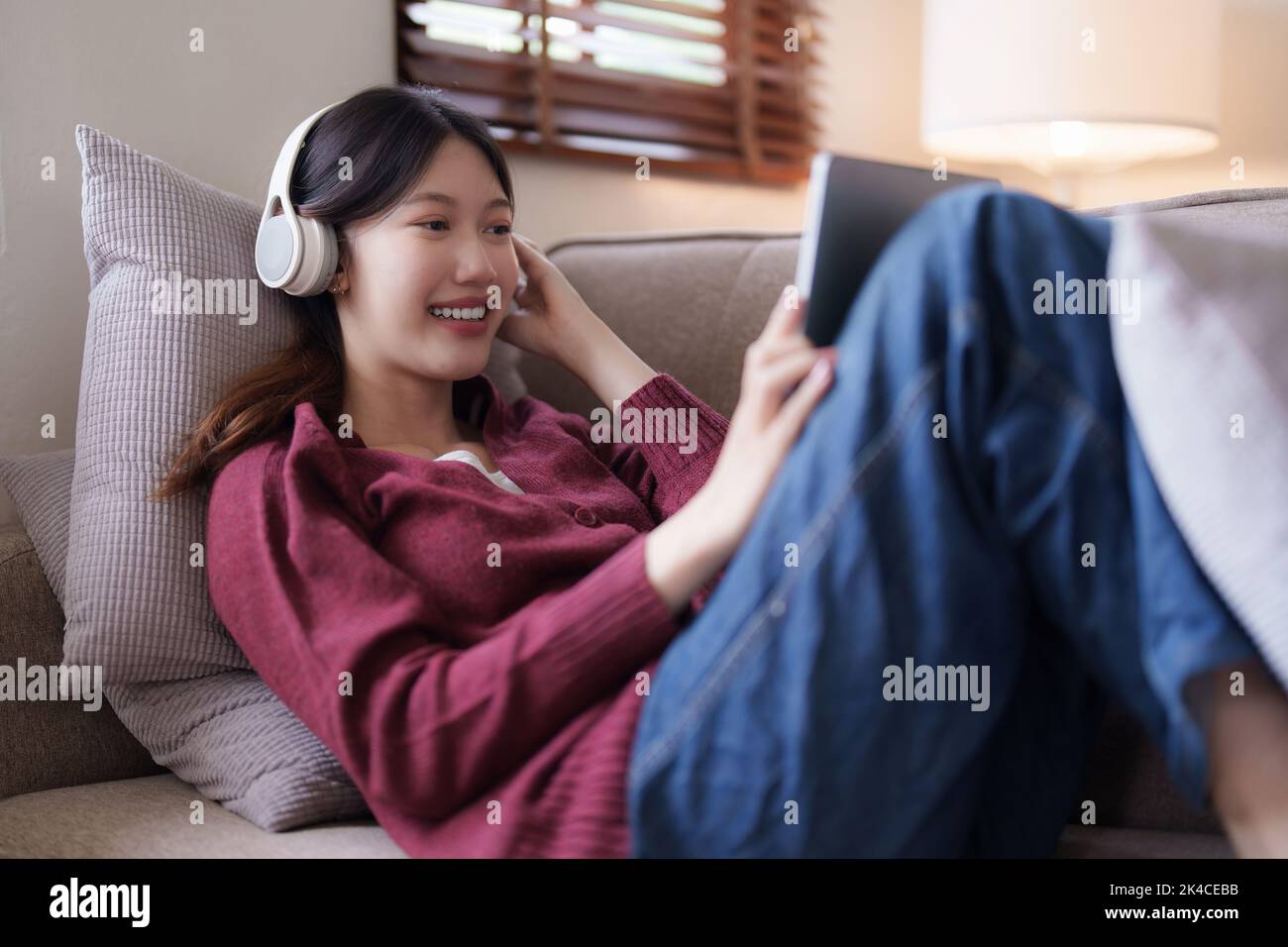 Attraktive lächelnde junge Frau mit Tablet und Musik hören auf dem Sofa zu Hause. Lifestyle-Konzept Stockfoto