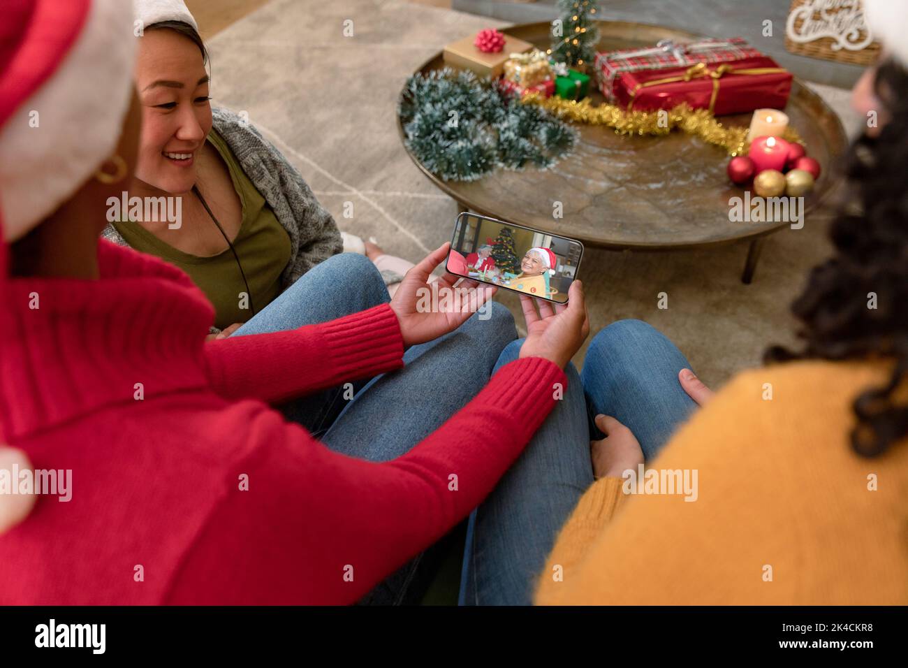 Fröhliche, vielfältige Gruppe von Freunden, die mit lächelnden älteren Freunden ein Weihnachtsvideo über das Smartphone führen. Weihnachten, Festlichkeiten und Kommunikationstechnik. Stockfoto