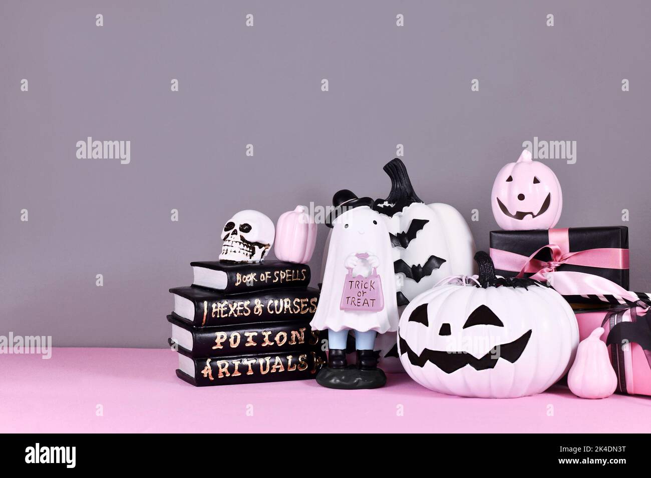 Pink-weißes Halloween-Dekor mit schwarzen und weißen Kürbissen, niedlichen Geisterbüchern und Zauberbüchern auf grauem Hintergrund Stockfoto