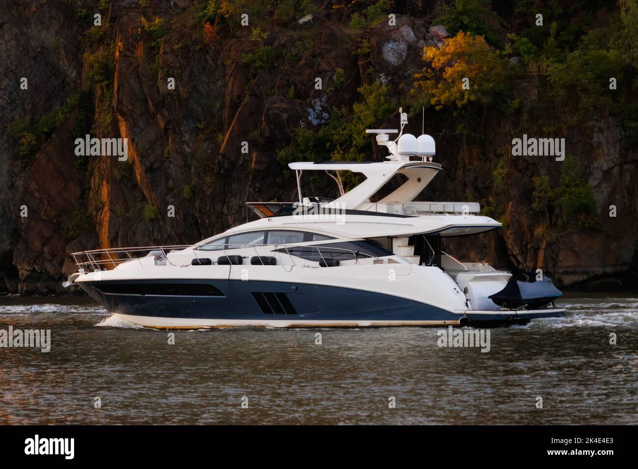Freizeityacht auf dem Hudson River im Sommer zur goldenen Stunde mit Klippen und Laub im Hintergrund, die das orangefarbene Sonnenlicht reflektieren Stockfoto