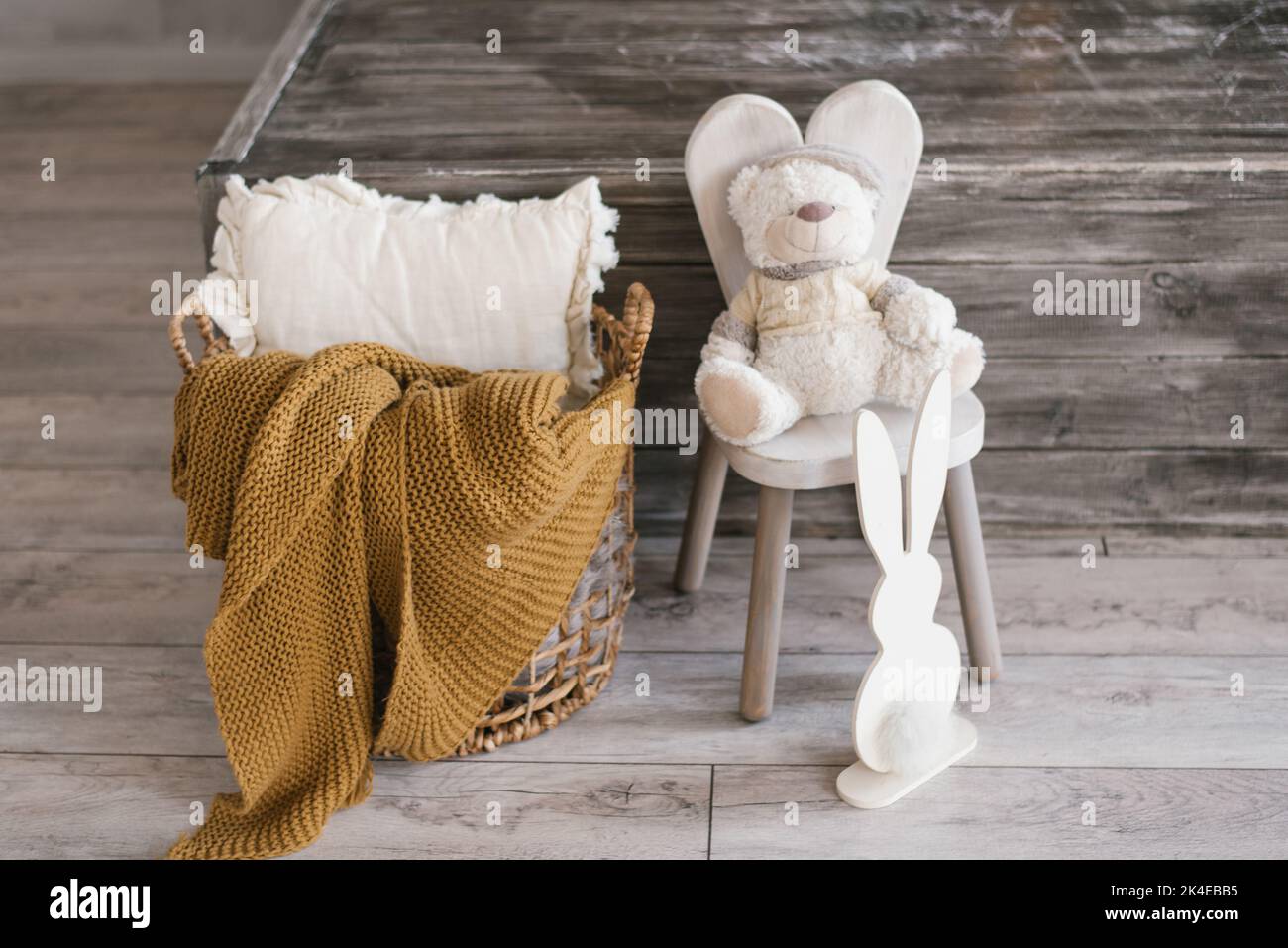 Der Plüschtier-Bär für Kinder sitzt auf einem Stuhl, daneben befindet sich ein Sperrholzhäschen und ein Korb mit einer Decke und einem Kissen. Accessoires im Sommerzimmer Stockfoto