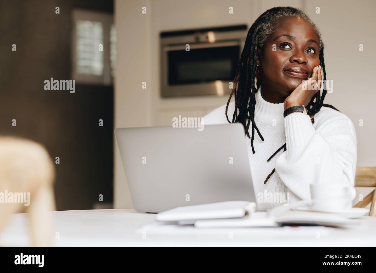 Eine Geschäftsfrau, die zu Hause an einem Laptop arbeitet, schaut nachdenklich weg. Reife Geschäftsfrau, die freiberufliche Online-Arbeit in ihrem Heimbüro macht. Stockfoto