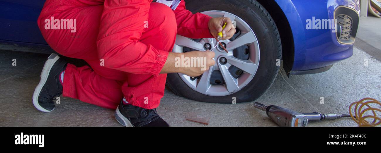 Reifenspezialist in seiner Werkstatt, während er ein durchbrochenes Rad eines Autos mit Pflaster und Kitt repariert. Machen Sie es selbst. Horizontales Banner Stockfoto