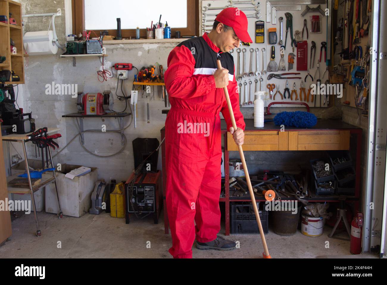 Bild eines Mechanikers, der mit einem Besen den Boden seiner Werkstatt fege. Stockfoto