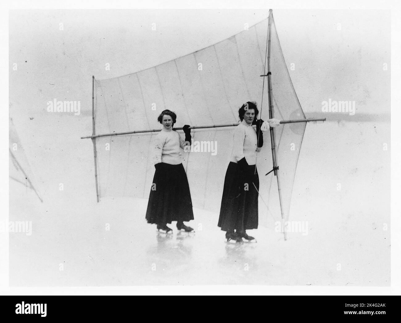 Schlittschuhlaufen auf Eis. Zwei Frauen in der damaligen Sportbekleidung, lange Röcke und Poloshirts und auf Schlittschuhen halten gemeinsam ein Skating-Segel hinter sich. Nordisch Stockfoto