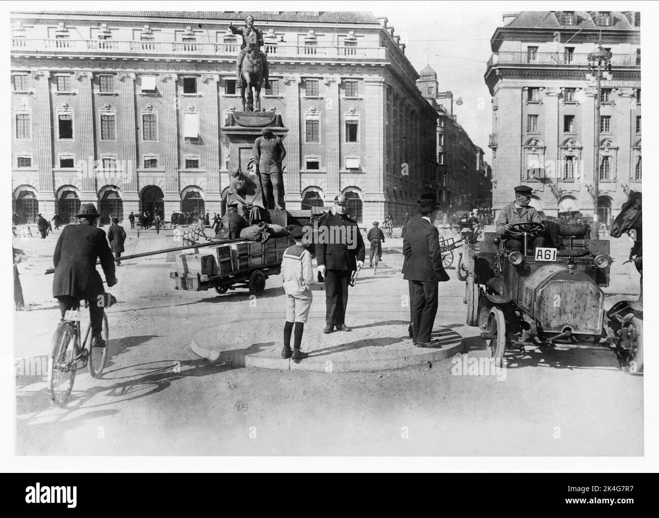 Stadtbild vom Gustav Adolf Platz in Stockholm, 1910. Mitten im Kreisverkehr steht ein Polizeibeamter, der den Verkehr überwacht, einige Männer in Anzug und ein Junge im Sjöman-Kostüm mit kurzen Hosen. Radfahrer, ein Auto und Pferdewagen sind auf der Straße versammelt. Im Hintergrund Gebäude und l'archevêques Statue von Gustav II Adolf. Nordisch Stockfoto