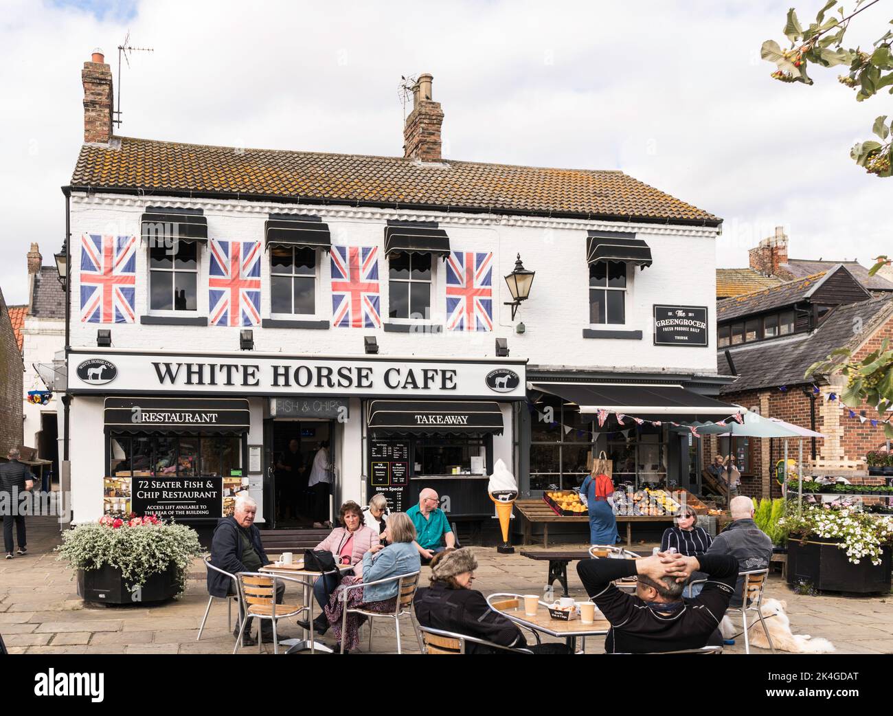 Menschen, die vor dem White Horse Café auf dem Thirsk Market Place, North Yorkshire, England, Großbritannien, sitzen Stockfoto