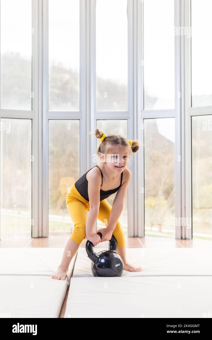 Nettes kleines Mädchen versucht, Kettlebell zu heben. Fitnessspaß Stockfoto