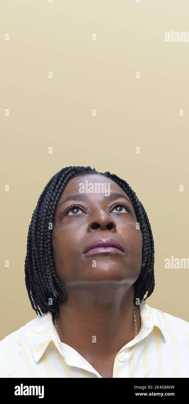 Afrikanische Frau, die auf schlichtem pastellfarbenem Hintergrund aufschaut Stockfoto