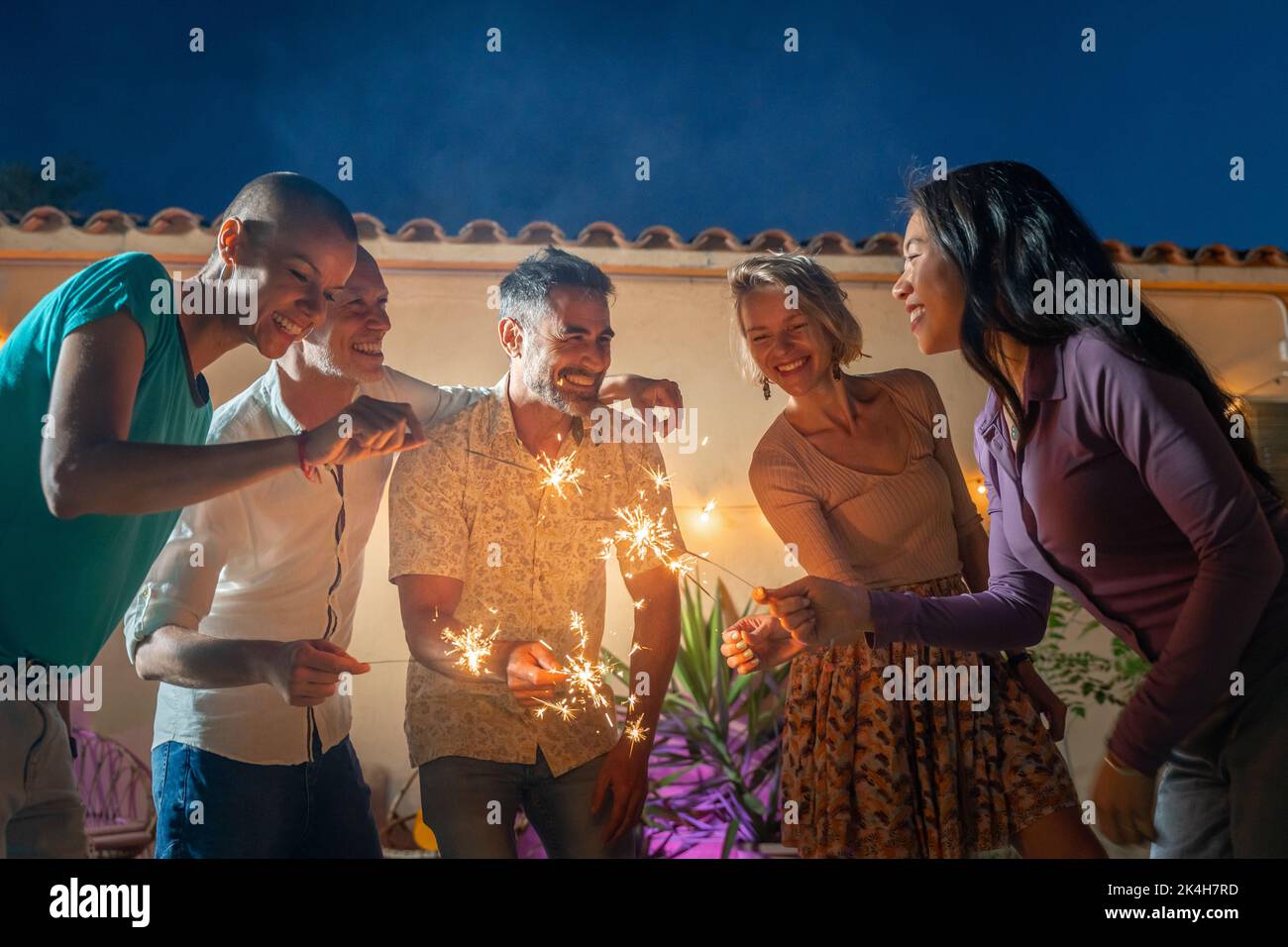 Reife Freunde feiern glücklich mit Funkeln in der Nacht. Fröhliche Menschen feiern in einem Nachtclub im Freien. Stockfoto