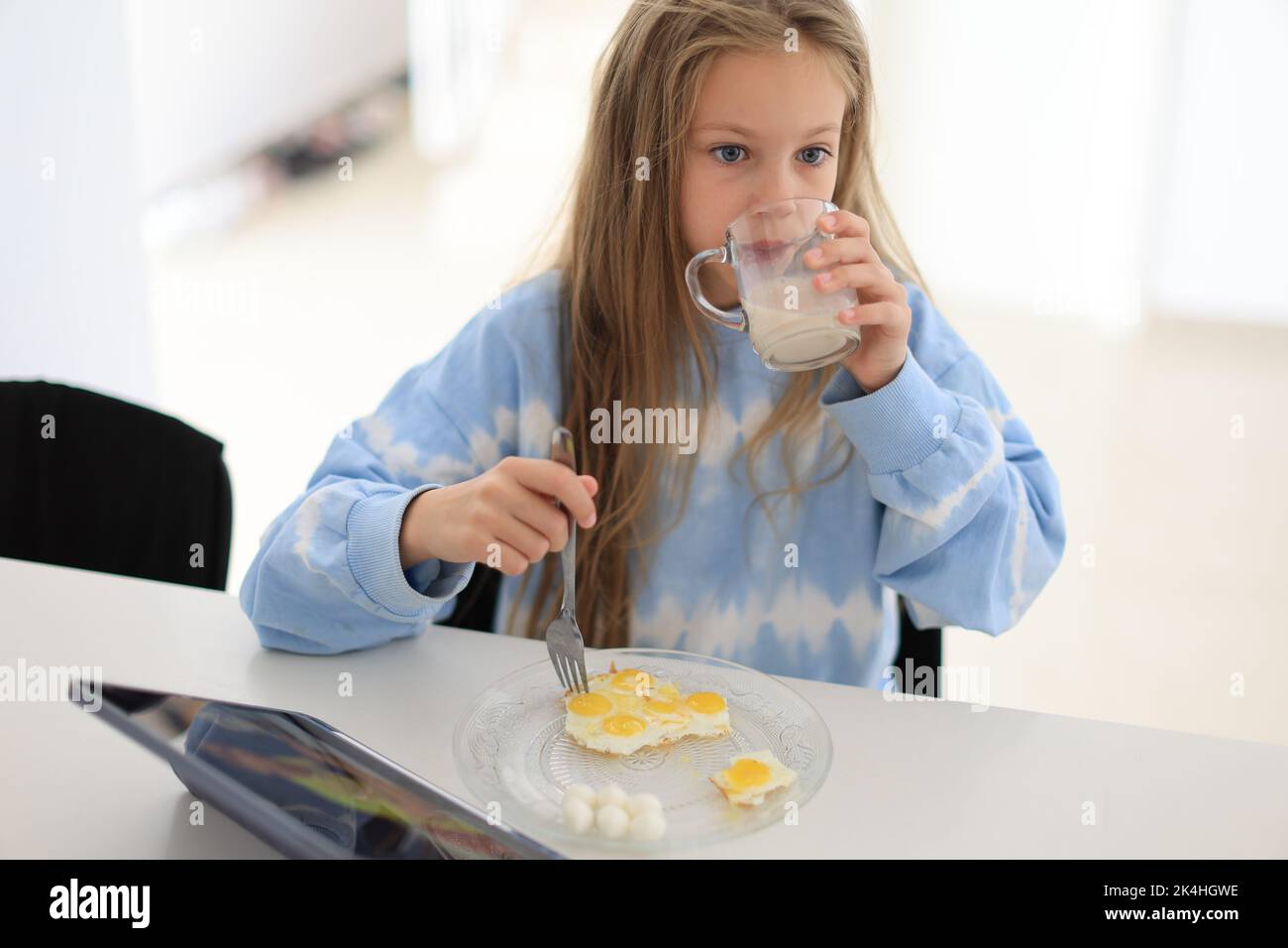 Das kleine Mädchen trinkt morgens Milch mit Ei und sitzt am Tisch. Richtige Ernährung für Kinder Stockfoto