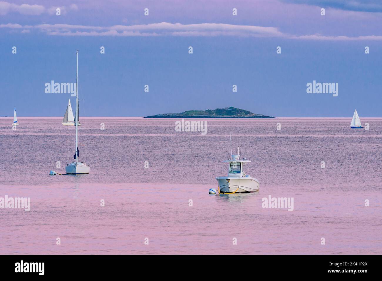 Boote im Kanal mit Insel im Hintergrund und rosa Wolken, die sich im Ozean spiegeln Stockfoto
