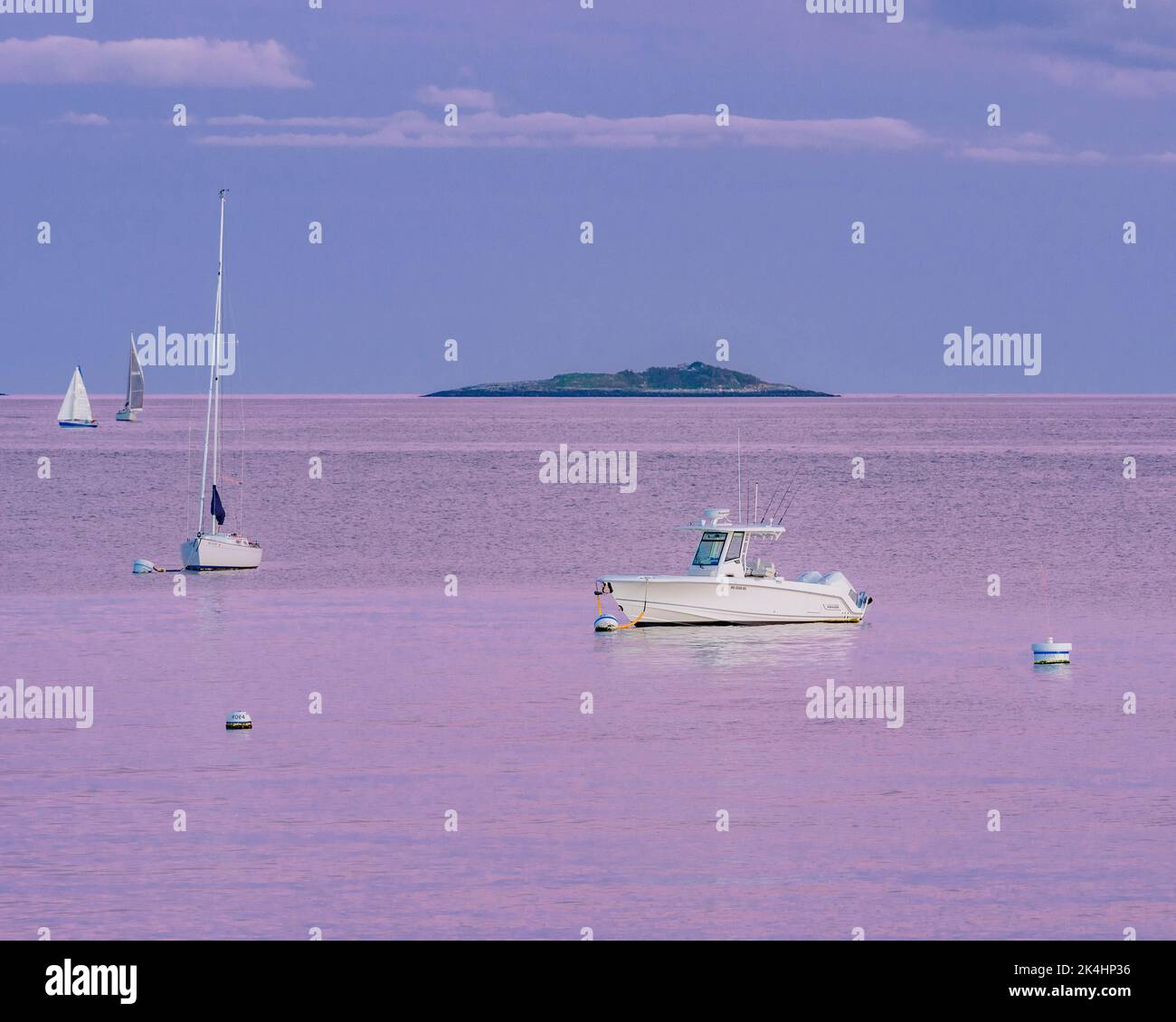 Boote im Kanal mit Insel im Hintergrund und rosa Wolken, die sich im Ozean spiegeln Stockfoto