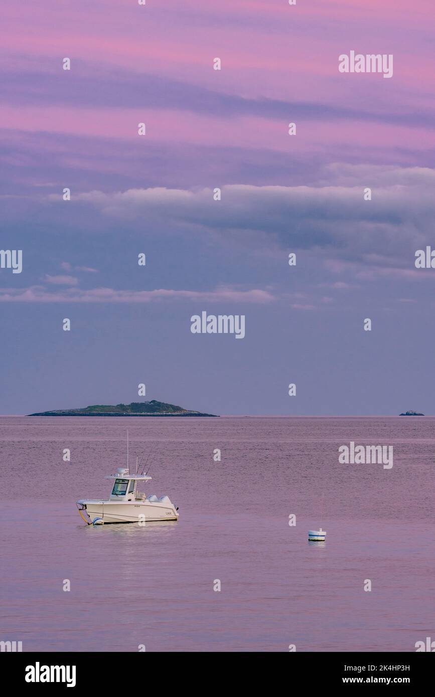 Das einfarbige Boot liegt im Kanal mit der Insel im Hintergrund und den rosafarbenen Wolken, die sich im Ozean spiegeln Stockfoto