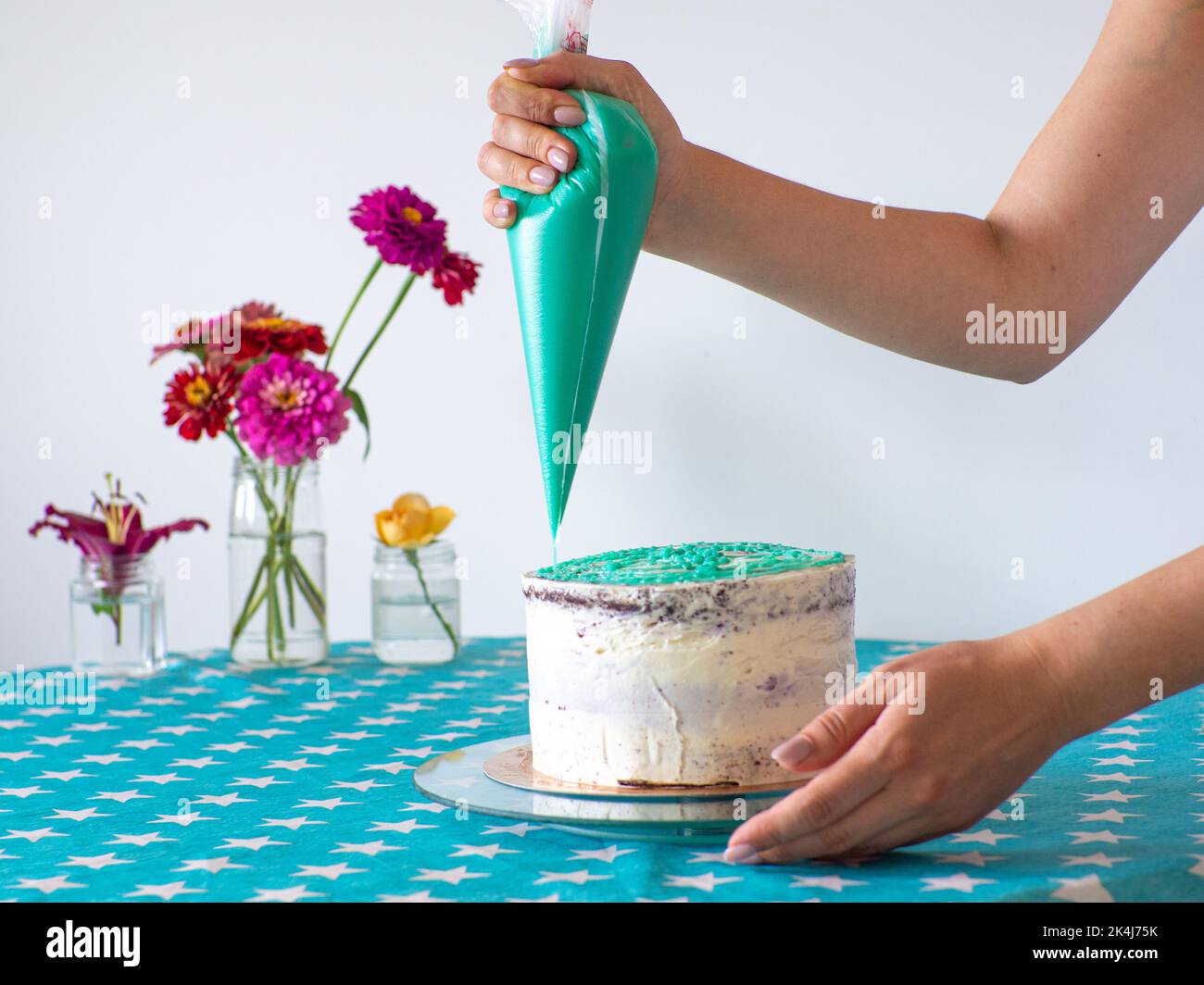 Hände heben die Creme mit einem Gebäckbeutel und bedecken den runden Kuchen Stockfoto