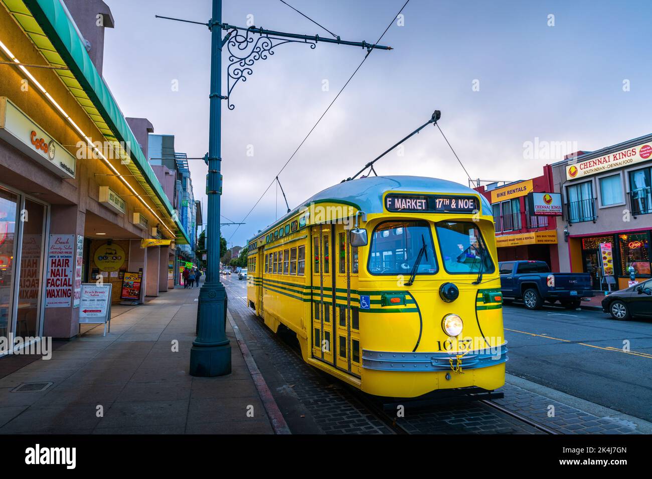 San Francisco, California, USA - 28. September 2019: Gelbe elektrische Busparks an der Fisherman Wharf Station bereit für den Service mit Hintergrund der Geschäfte i Stockfoto