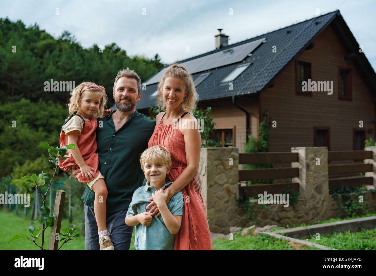 Glückliche Familie in der Nähe ihres Hauses mit Sonnenkollektoren. Alternative Energie, Ressourcenschonung und nachhaltiges Lifestyle-Konzept. Stockfoto