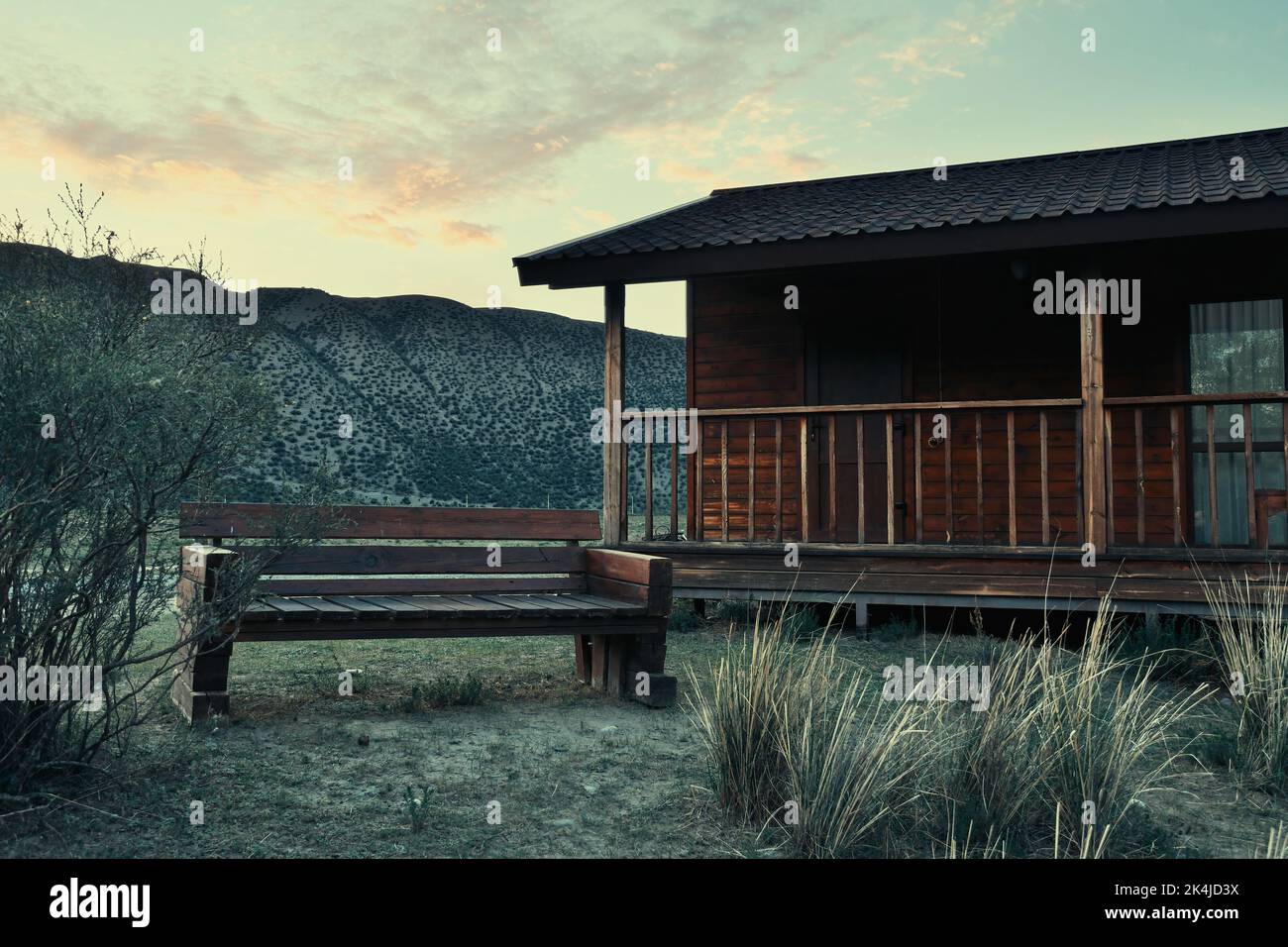 Einsame ländliche Hütte und Bank in der Steppe mit Bergen. Einsamkeit Konzept in Natur und Architektur Stockfoto