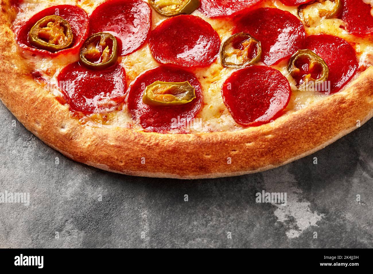 Pizza mit geschmolzenem Mozzarella, Tomatensauce, Pepperoni und Jalapeno auf grauem Stein Stockfoto