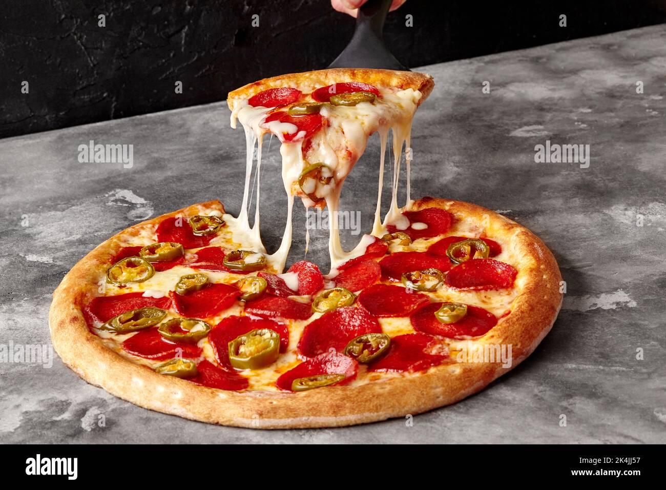 Scheibe Pepperoni-Pizza mit geschmolzenem Mozzarella und Jalapeno auf dem Servierspatel Stockfoto
