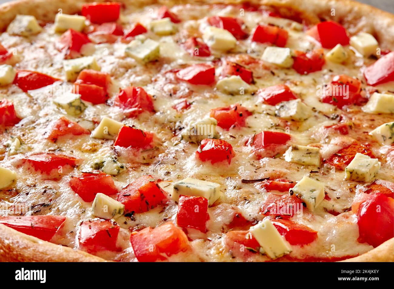 Nahaufnahme von Pizza mit Tomaten und Blauschimmelkäse auf geschmolzenem Mozzarella mit getrockneten Kräutern Stockfoto