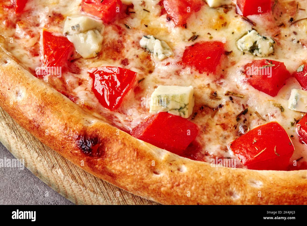Nahaufnahme von Pizza mit Mozzarella, Tomaten, Blauschimmelkäse und getrocknetem Basilikum auf Holzbrett Stockfoto