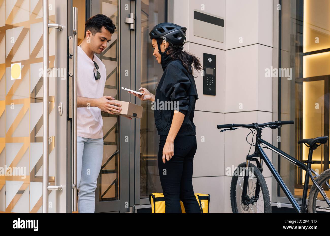 Frau, die als Kurierin arbeitet. Eine Frau, die den Barcode einscannt, während der Kunde einen Karton in der Hand hält. Stockfoto