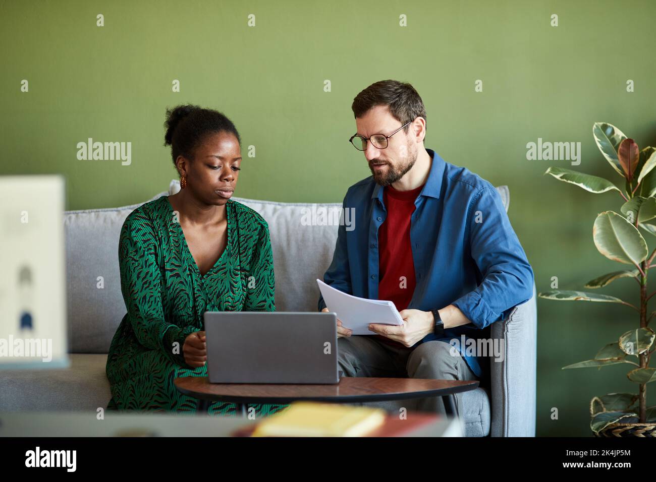 Der junge Geschäftsmann und sein afroamerikanischer Kollege in intelligenter Casualwear sehen und diskutieren Online-Videos bei einem Treffen im Büro Stockfoto