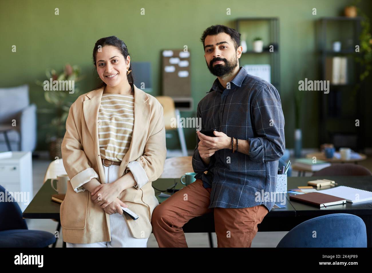Zwei junge, erfolgreiche Designer oder Angestellte in eleganter Casualwear, die am Arbeitsplatz stehen und die Kamera betrachten Stockfoto