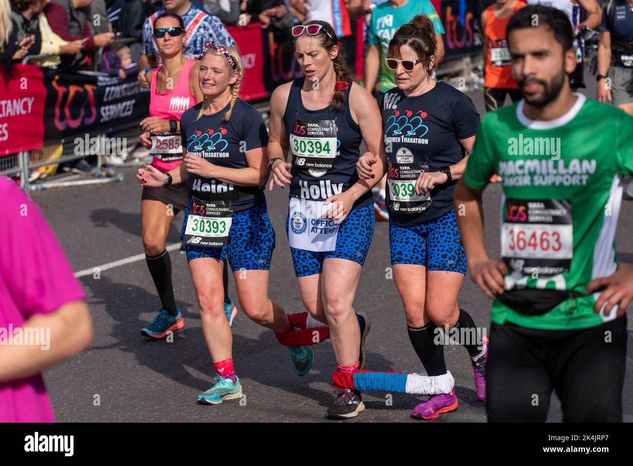 Vierbeinige Frauen, die beim TCS London Marathon 2022 auf der Tower Hill Road, City of London, Großbritannien, laufen. Mädchen gebunden zusammen Spaß laufen Stockfoto