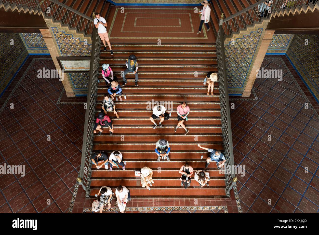 Erschöpfte Touristen sitzen an einem heißen Sommertag auf einer Treppe an der Plaza de España. Sevilla, Andalusien, Spanien. Stockfoto