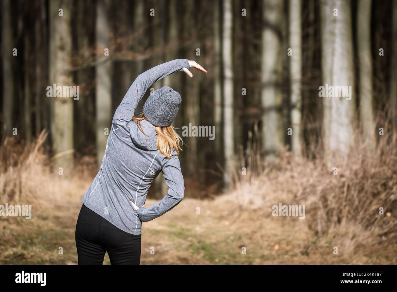 Frau dehnt sich vor dem Laufen im Herbstwald. Aufwärmübung. Wohlbefinden der Person während der Fitness Stockfoto