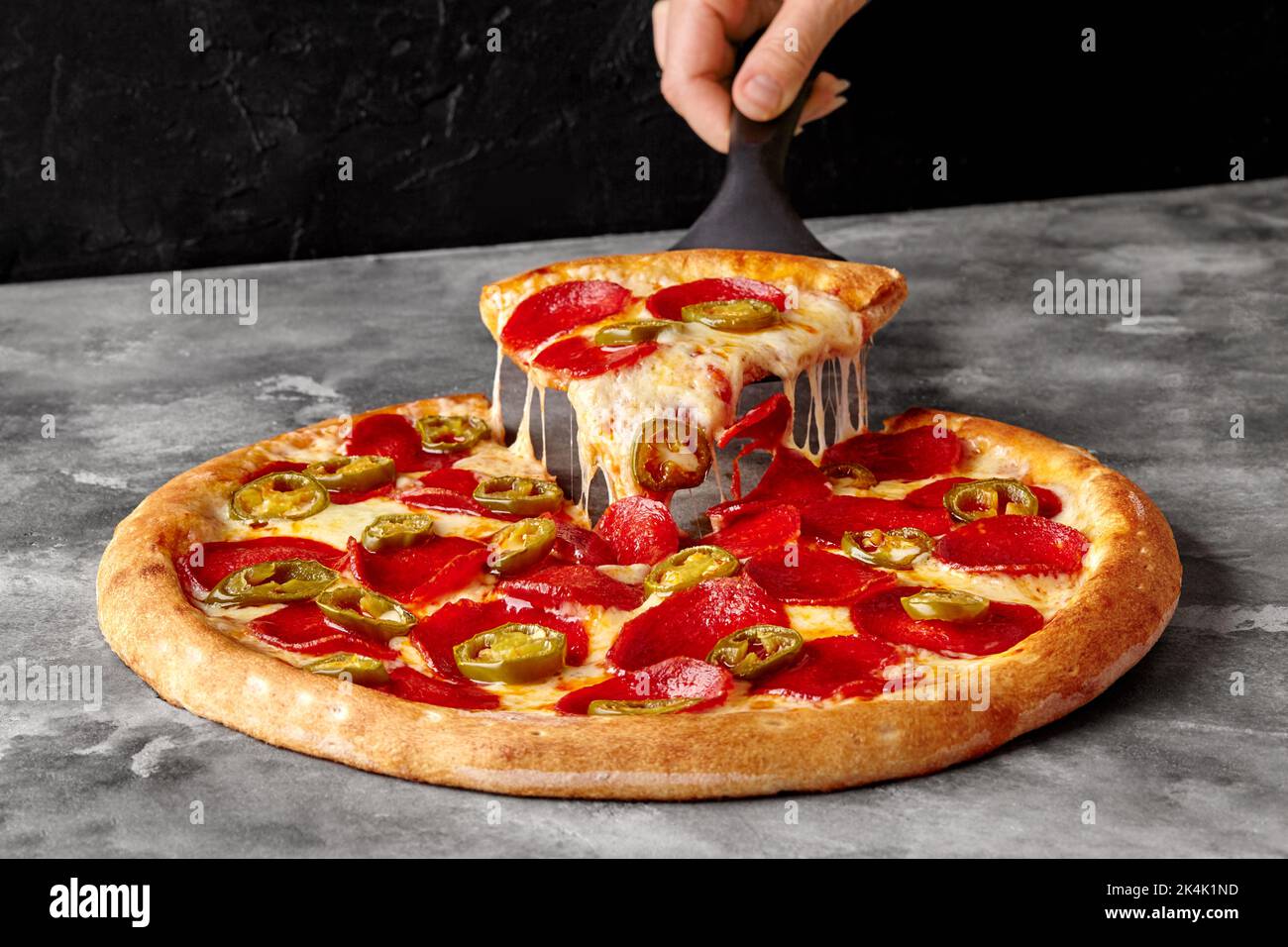 Weibliche Hand halten Servierpaddel mit Scheibe Pepperoni Pizza mit geschmolzenem Käse und Jalapeno Stockfoto