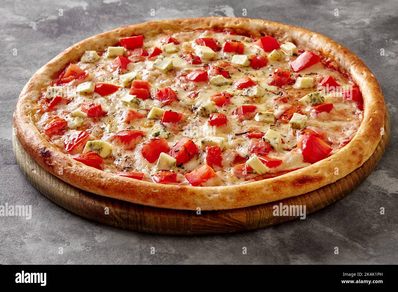 Pizza mit Mozzarella, Tomaten, Blauschimmelkäse und getrocknetem Basilikum auf einem hölzernen Servierbrett Stockfoto