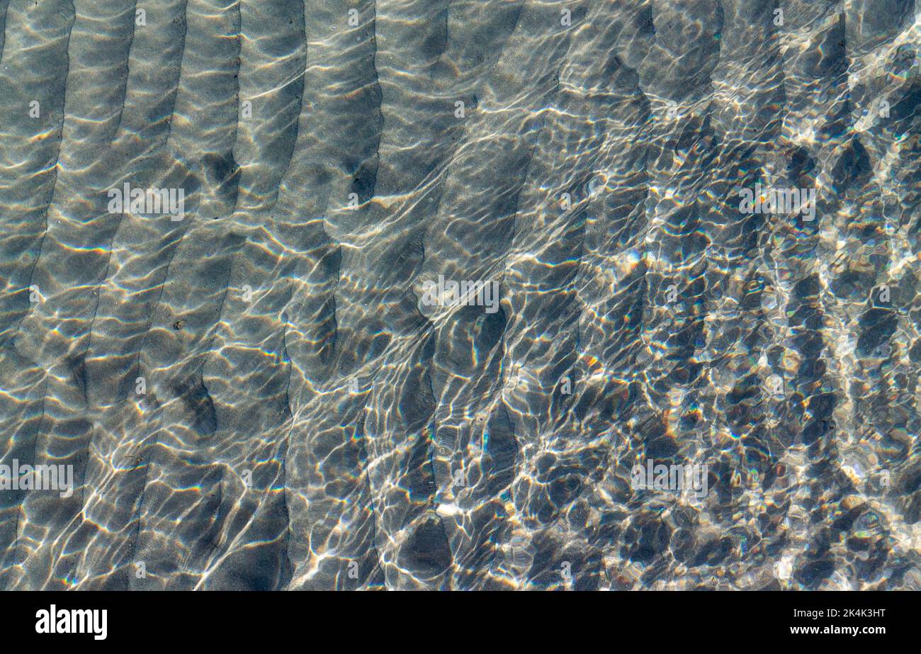 Sandiger Meeresboden oder Meeresboden, der durch klares Meerwasser gesehen wird und auf der Meeresoberfläche Sonnenlicht reflektiert wird. Stockfoto
