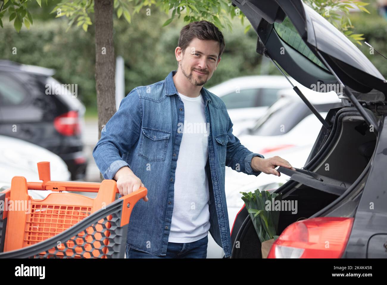 Lächelnder Mann, der Einkaufstasche in den Kofferraum des Autos legt Stockfoto