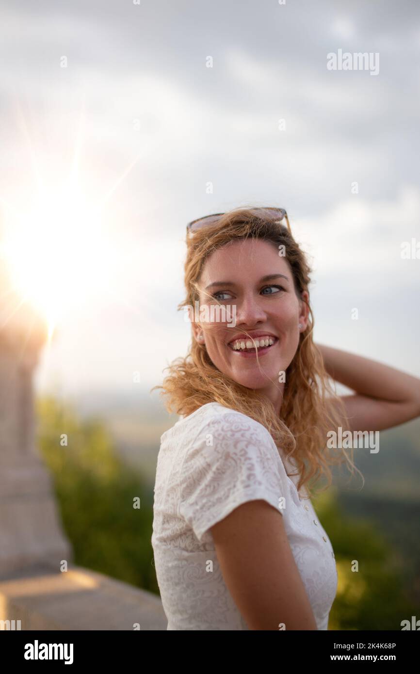 Glückliche junge 30s kaukasische Frau mit lockigen Haaren lacht bei Sonnenuntergang im Freien Stockfoto