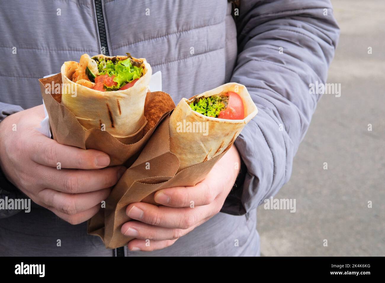 Shawarma zum Mitnehmen. Gebratenes Fleisch mit Gemüse und Sauce. Fastfood zum Mittagessen. Die Hand hält zwei frische Fleischsorten in Pitabrot. Stockfoto