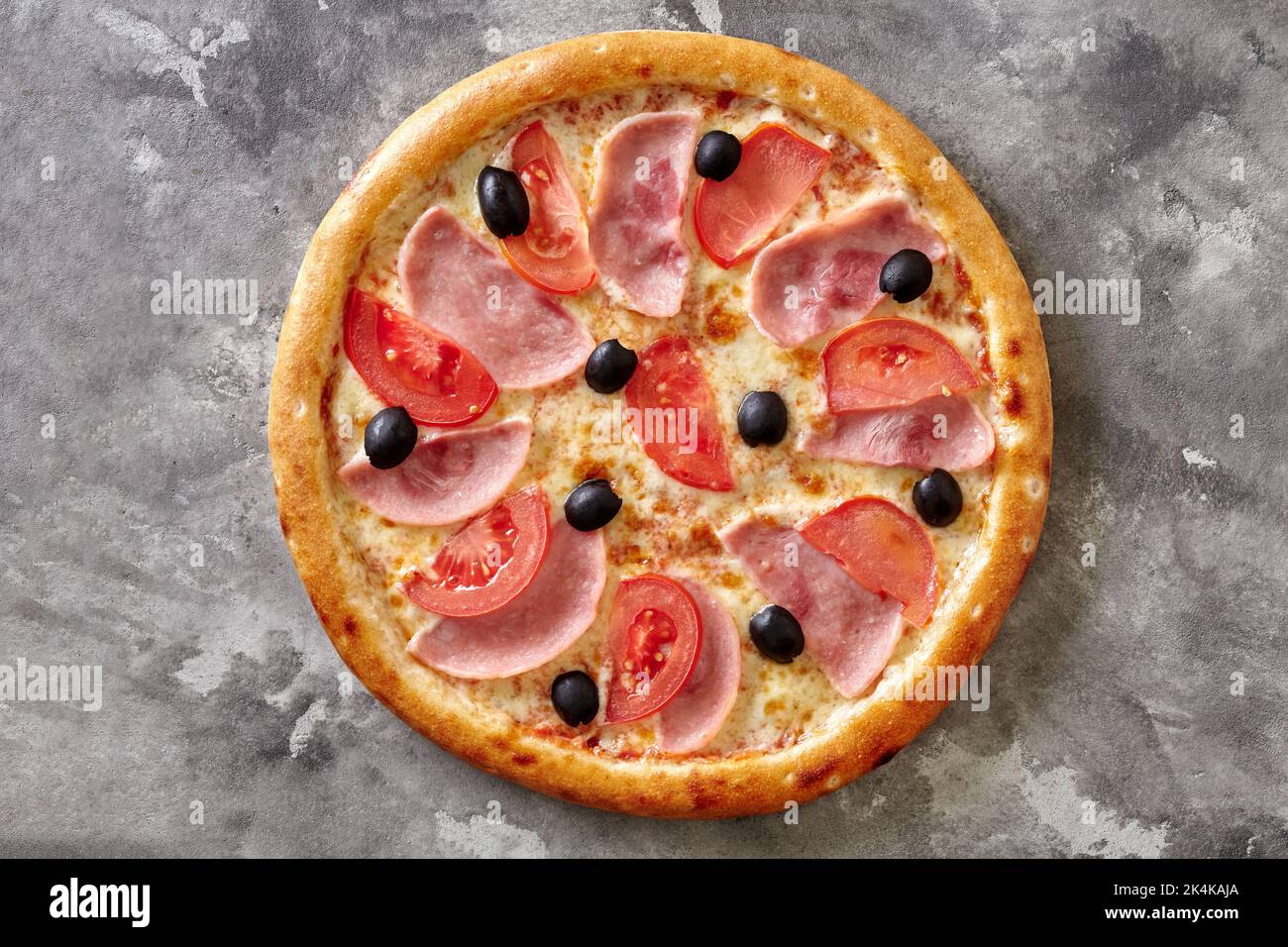 Dünne klassische Pizza mit geschmolzenem Käse, Schinken, Tomaten und schwarzen Oliven auf grauer Steinoberfläche Stockfoto