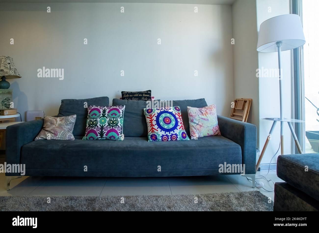 Grauer Stoffsessel, Wohnzimmer mit Fernseher, Holzmöbel und grauem Teppich, mexikanische Dekorkissen, Kissen und Lampe Stockfoto