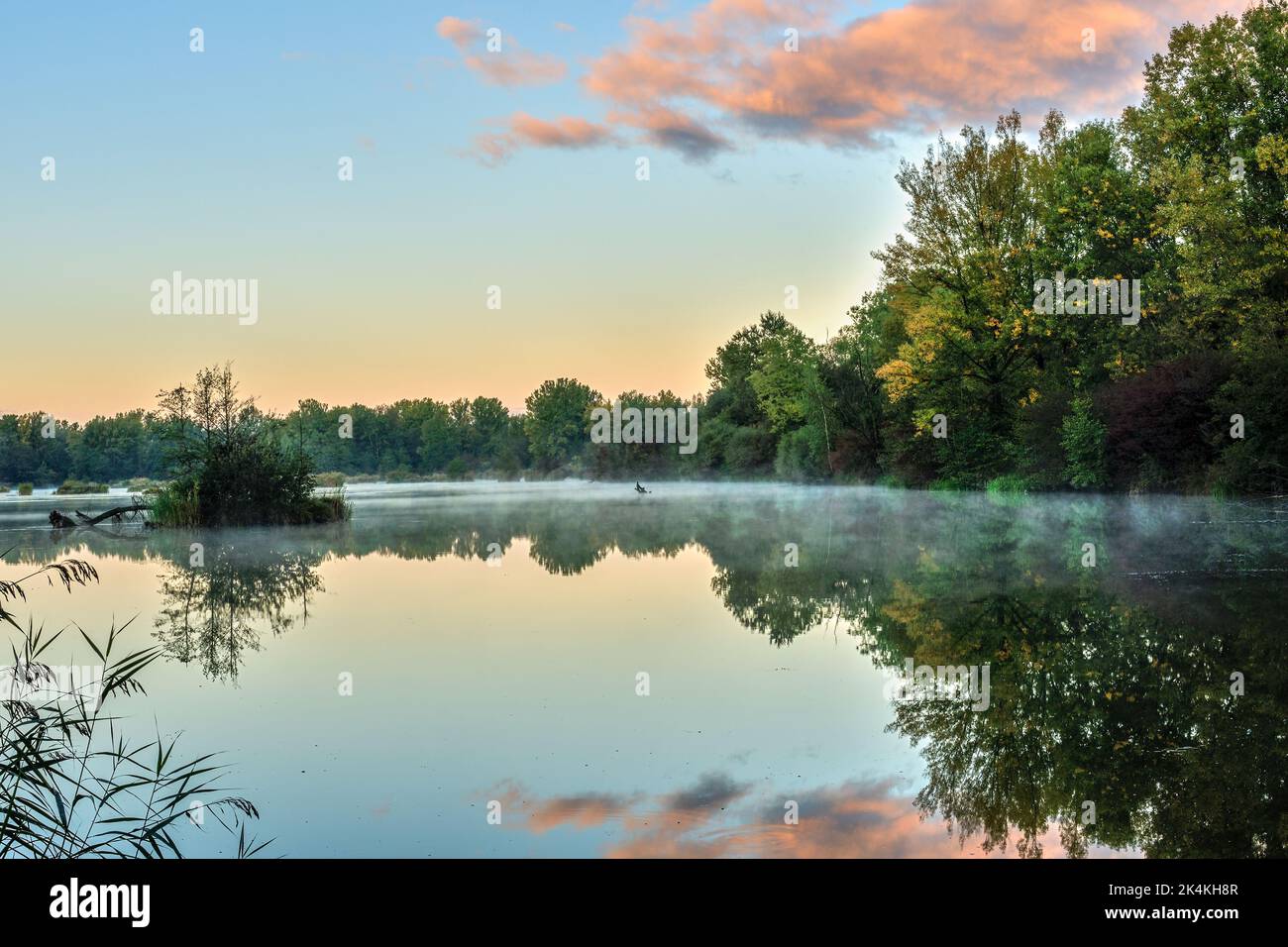 See bei Sonnenaufgang mit blauem Himmel und orangefarbener Wolke, ruhige Wasseroberfläche mit Dunst. Spiegelung. Herbstlandschaft, Natur Europas. Dubnica, Slowakei. Stockfoto