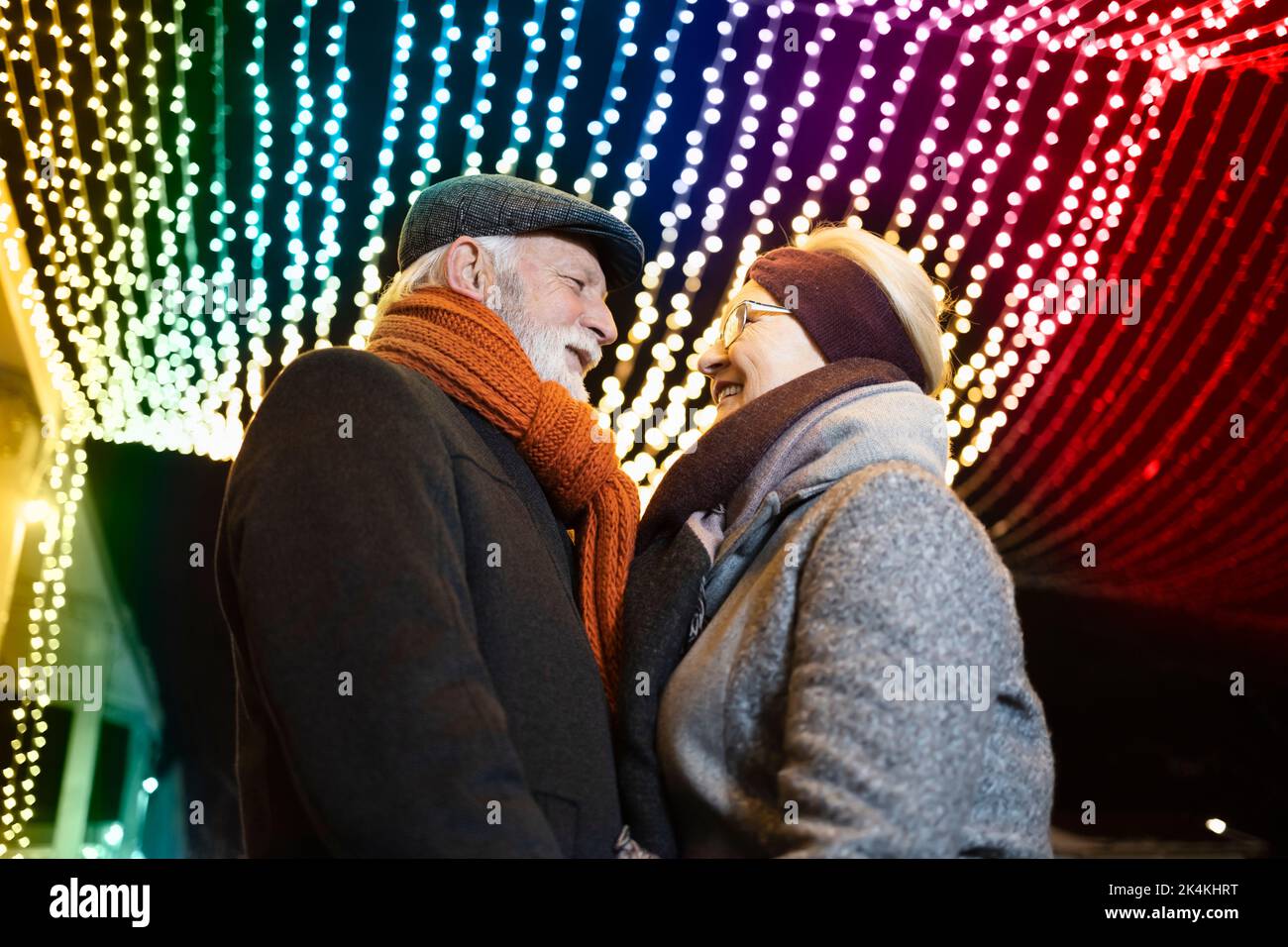 Ältere Paare in romantischer Umarmung unter den bunten Weihnachtslichtern Stockfoto