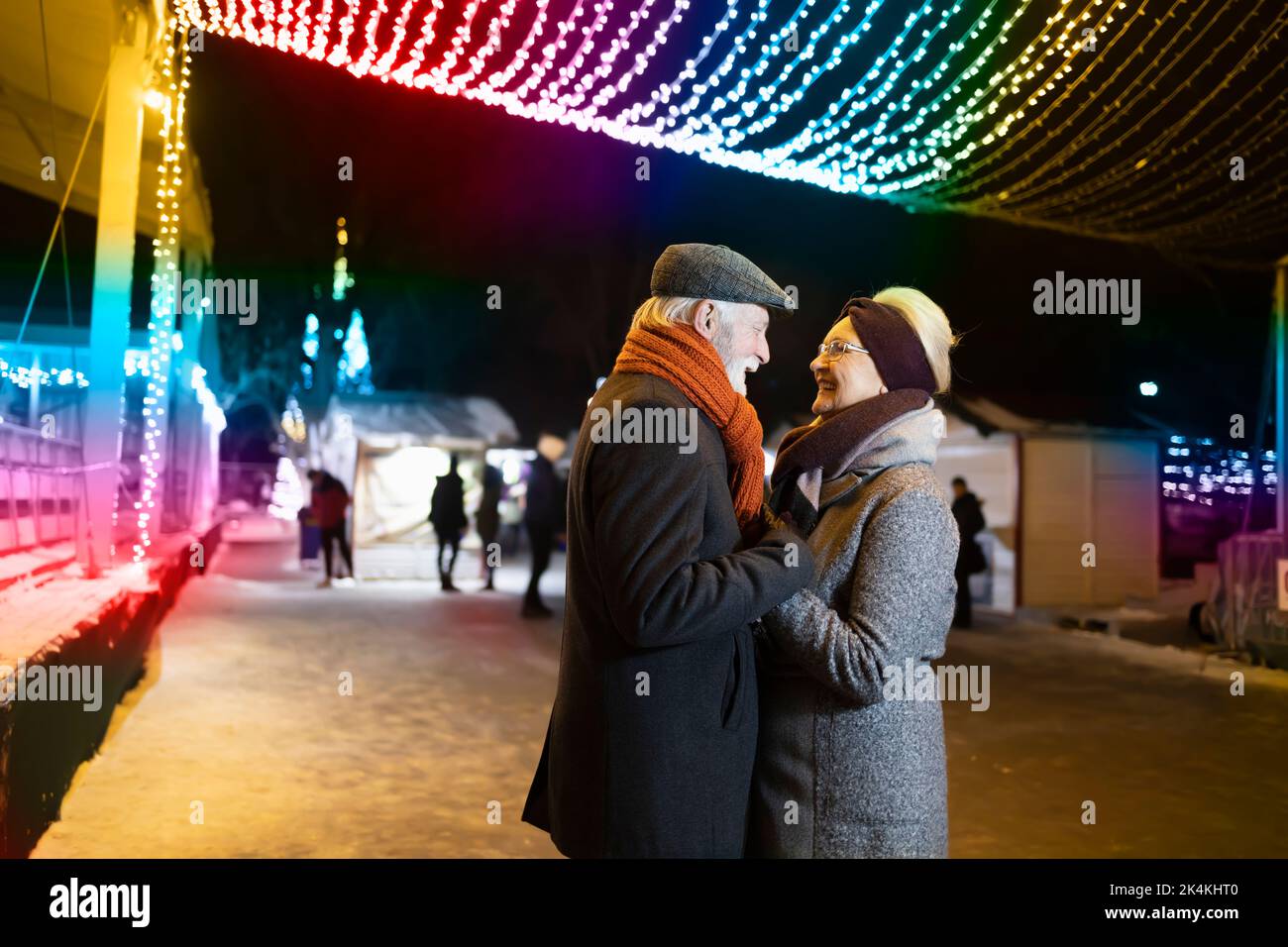 Glückliches älteres Paar, das die Hände hält und sich unter den Weihnachtslichtern wohlfühlt Stockfoto