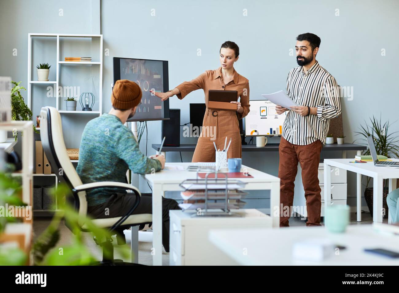 Junge, selbstbewusste Geschäftsfrau in eleganter Casualwear, die auf den interaktiven Bildschirm zeigt, während sie grafische Daten präsentiert Stockfoto