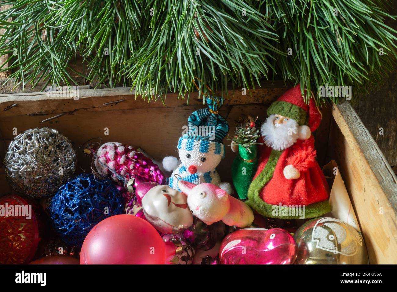 Ein Haufen alter Spielzeuge für den Weihnachtsbaum. Helle Objekte unter grünen Ästen aus der Nähe Stockfoto