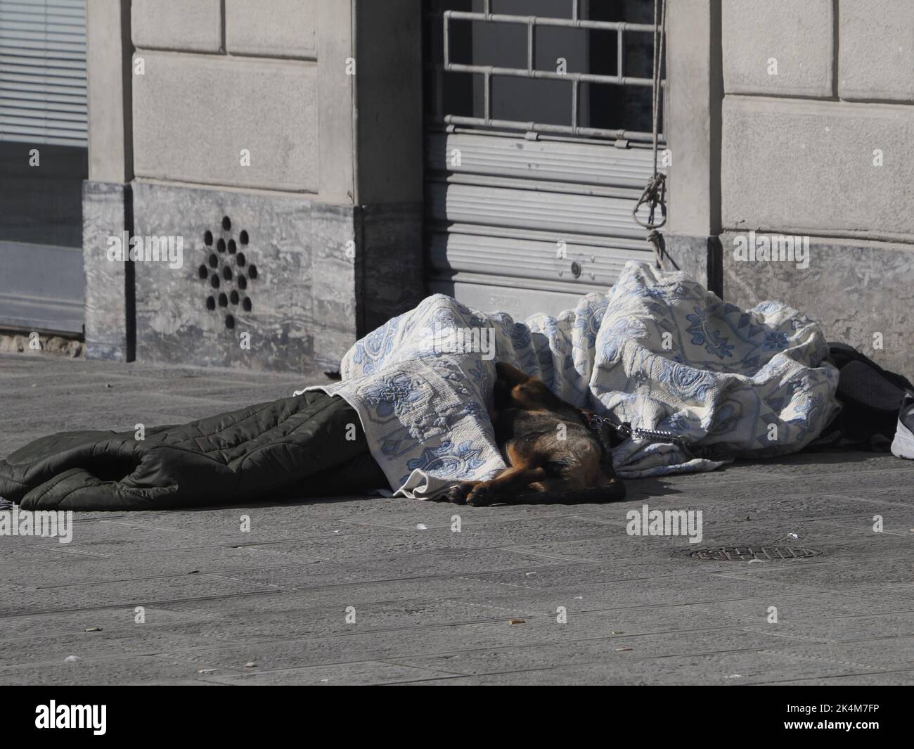 Eine Obdachlose, die tagsüber mit einem Hund auf einem öffentlichen Platz schläft Stockfoto