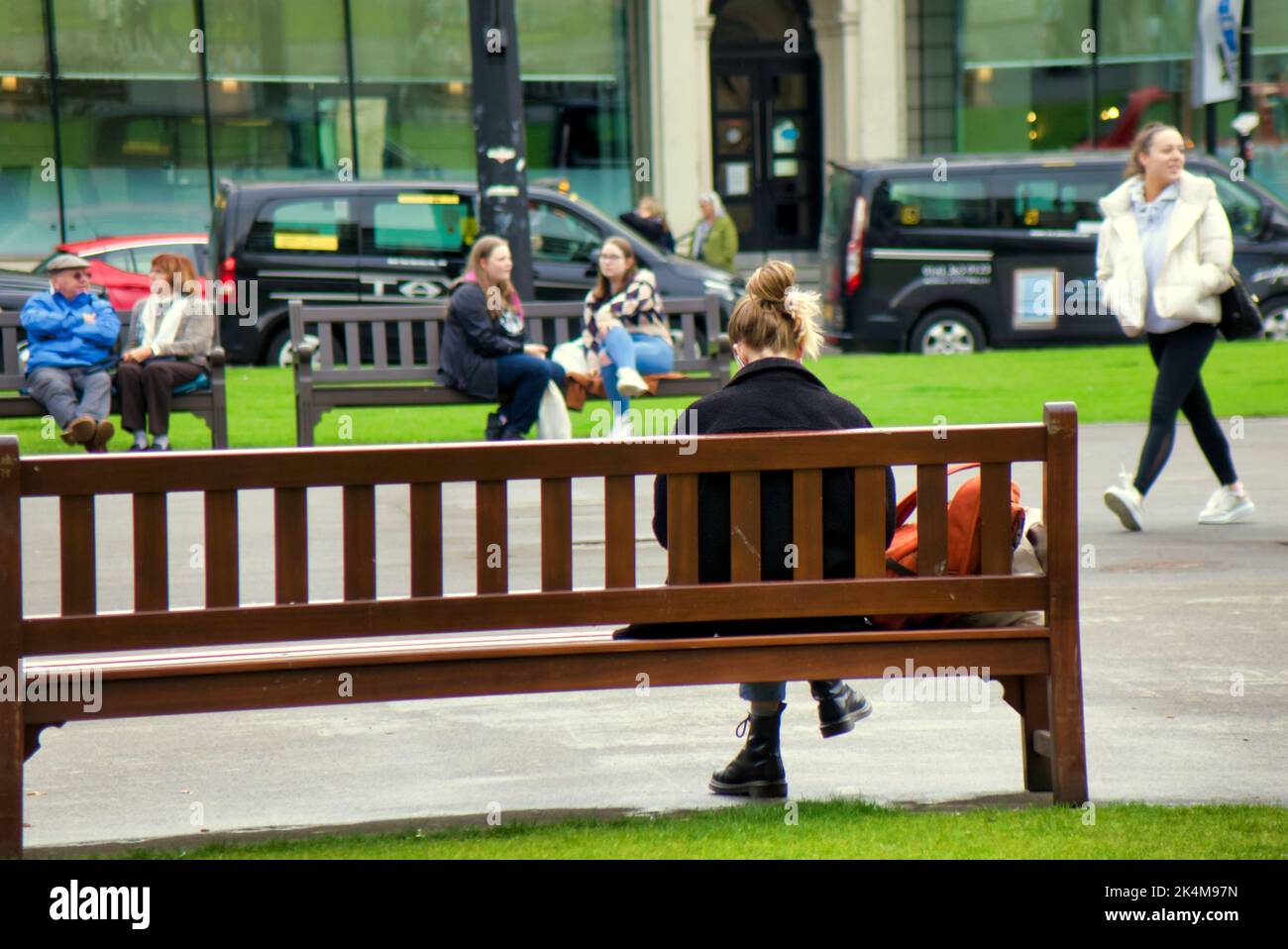 Junges Mädchen, das auf der Bank im george Square in Glasgow, Schottland, Großbritannien, sitzt Stockfoto