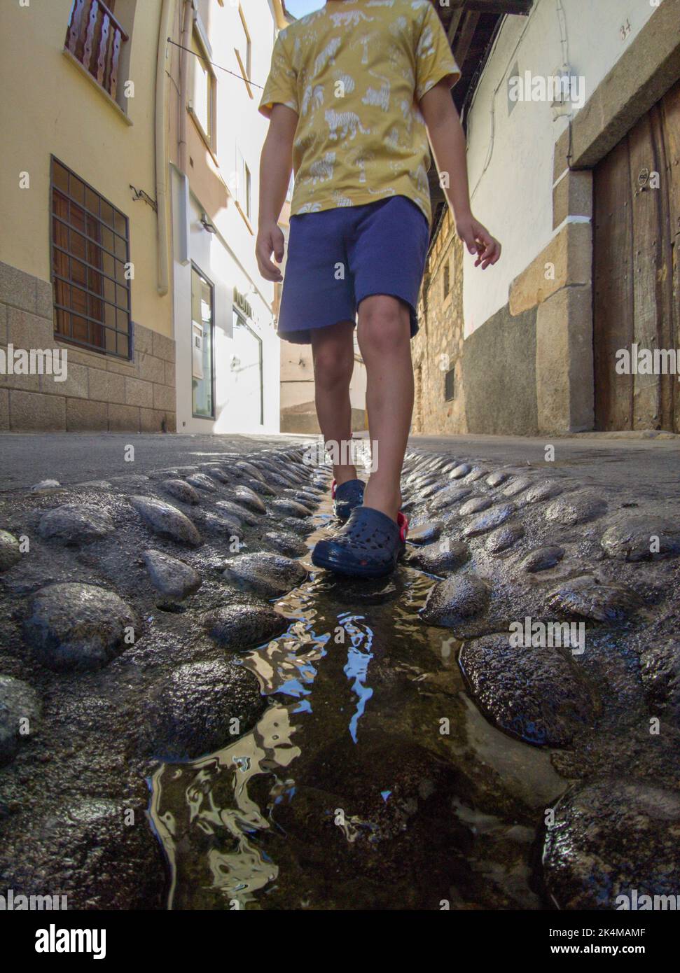 Kind, der am Straßenwasserkanal in Losar de la Vera, Caceres, Extremadura, Spanien, läuft. Stockfoto