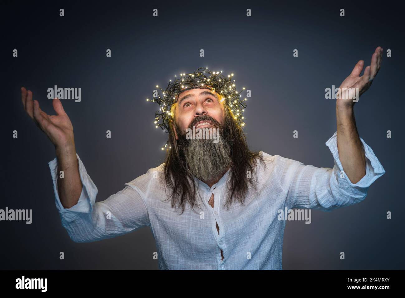 Mann mit Krone aus LED-Lichtern und erhobenen Armen mit Bart und langen Haaren Stockfoto